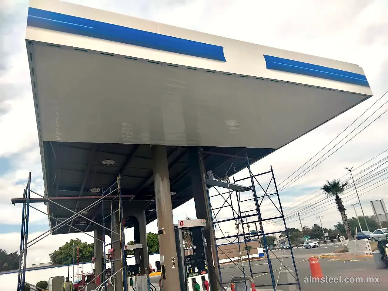 Plafón gasolinero blanco colocado bajo la techumbre, con andamios entre las bombas